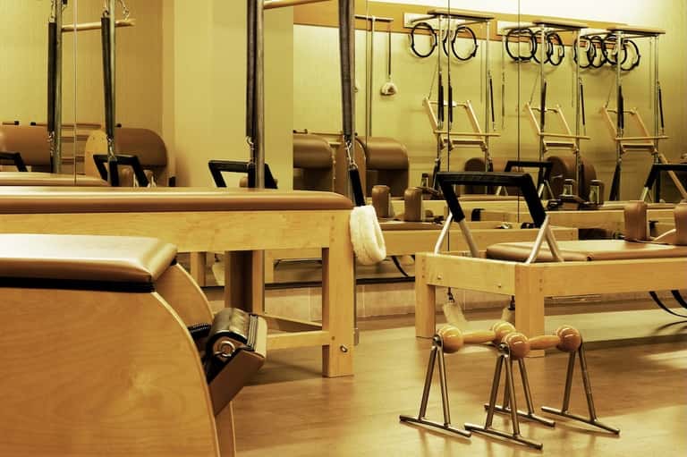 Pilates studio with reformer machines, mirrors, and wooden equipment in bright room
