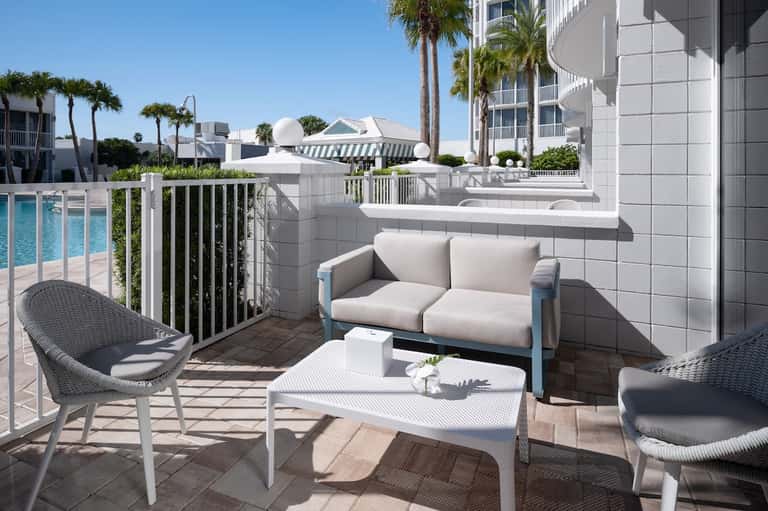 Beachfront hotel balcony with comfortable seating, ocean view, and palm trees