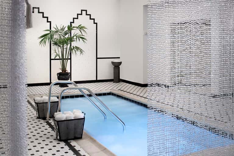 Indoor spa pool with geometric wall design, glass tiles, and tropical plant decoration