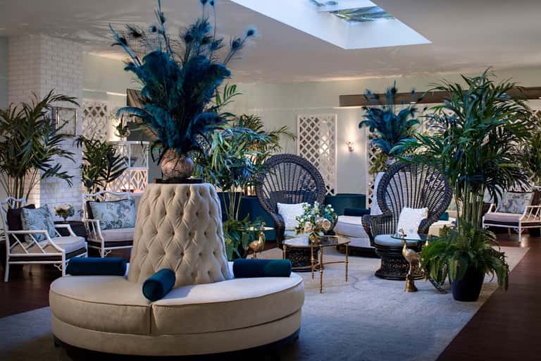 Upscale resort atrium with curved white seating, tropical plants, and rattan lounge chairs