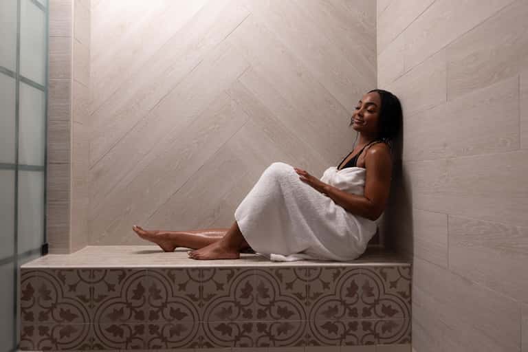 Woman relaxing in modern spa niche with white towel and decorative tile detailing on walls