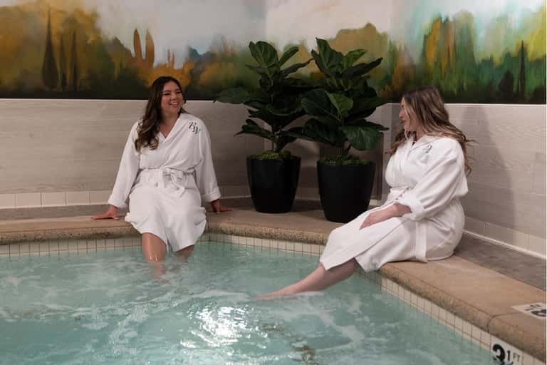 Spa hot tub with two women in white robes and potted plants indoors