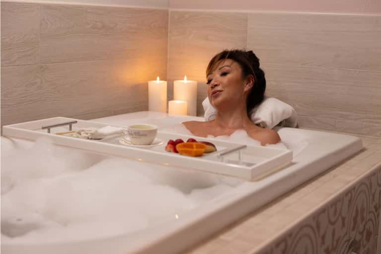 Woman relaxing in spa bath with candles and bath amenities on wooden tray