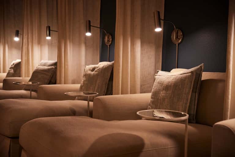 Luxury spa relaxation lounge with beige recliners, warm lighting, and curtained privacy spaces