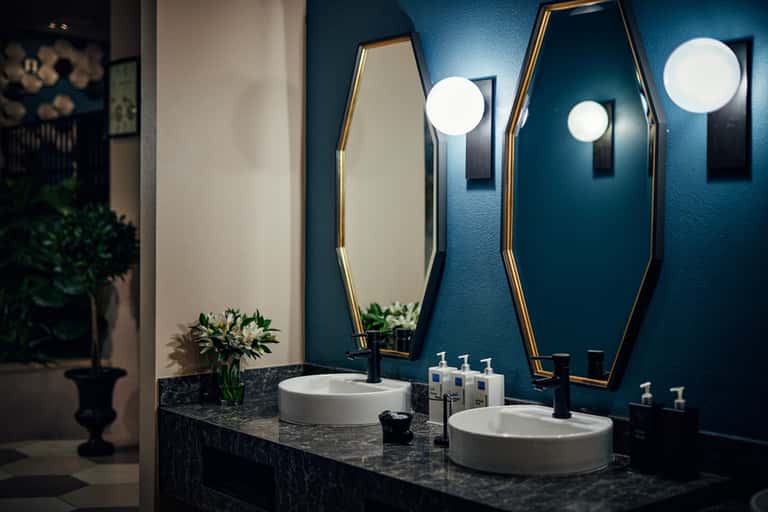 Luxury bathroom with teal accent wall, coffin-shaped mirrors, dual sinks, and ambient lighting