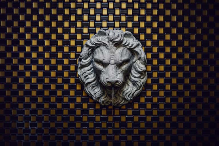 Decorative stone lion head sculpture mounted on geometric gold and navy blue tiled wall panel