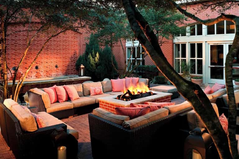 Courtyard fireplace lounge with orange cushioned seating, brick building, fire pit, and candlelight at dusk