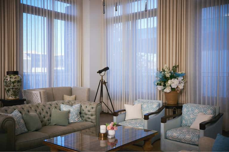 Elegant sitting room with green tufted sofa, armchairs, telescope, white flowers, and floor-to-ceiling sheer curtains