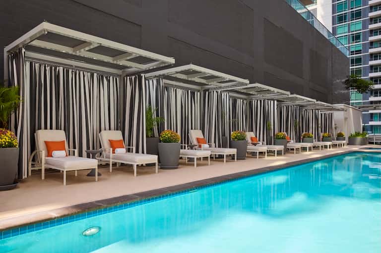 Luxurious pool cabanas with striped curtains and loungers beside a sparkling swimming pool