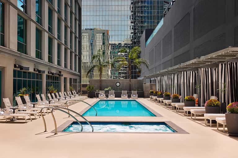 Urban hotel courtyard pool surrounded by white lounge chairs and high-rise buildings