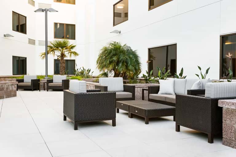 Outdoor courtyard with modern rattan furniture, white cushions, palm trees, and contemporary architecture
