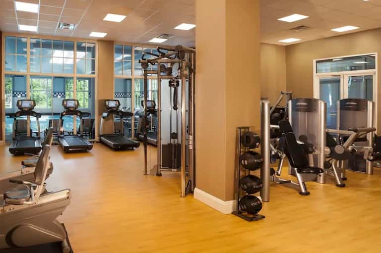 Bright fitness center with exercise equipment, large windows, yellow floors, and mirrored walls