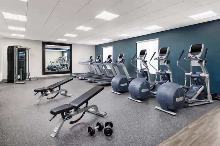 Contemporary fitness center with cardio equipment, dumbbells, and blue accent wall