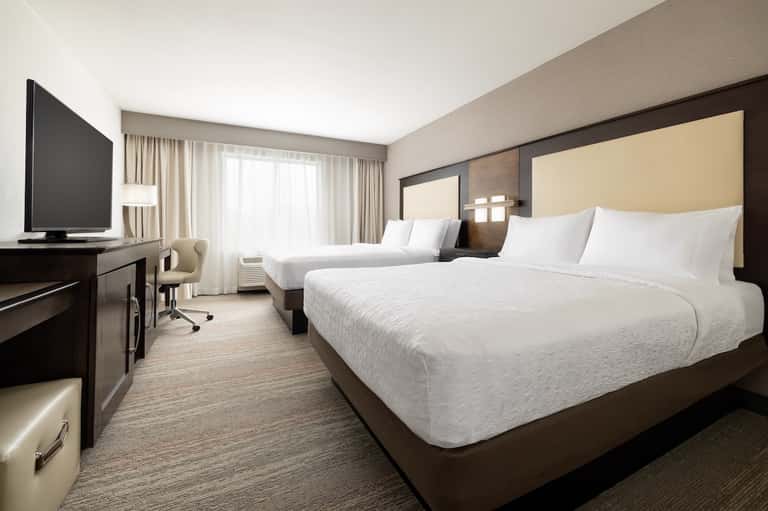Modern hotel room with two queen beds, desk, TV, and contemporary furnishings