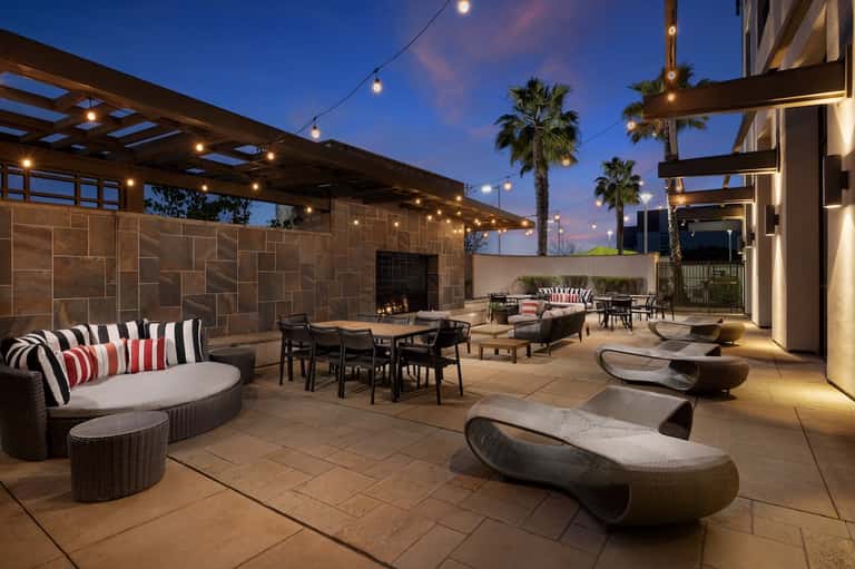 Upscale courtyard patio with modern seating, woven furniture, fireplace, and evening ambient lighting