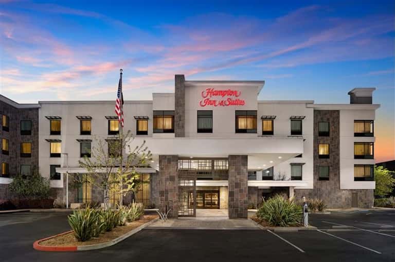 Hampton Inn & Suites exterior at dusk with lit windows, white facade, stone accents, and entrance