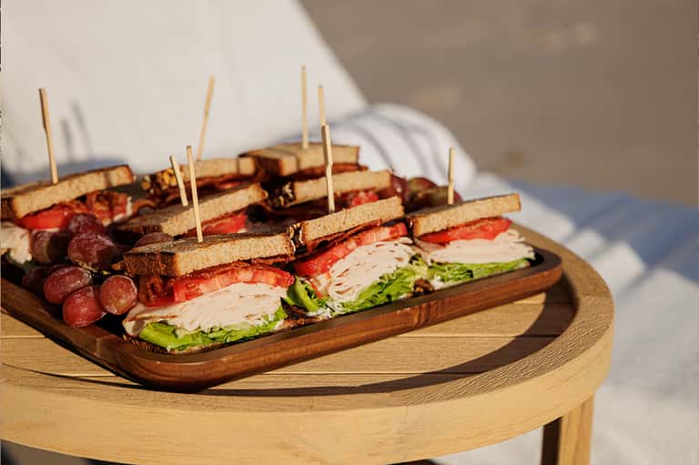 Gourmet appetizer platter with sandwiches, cured meats, and garnishes on wooden board