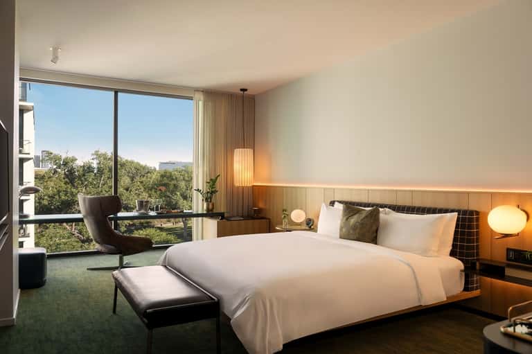 Luxury hotel bedroom with modern furnishings, floor-to-ceiling windows with nature views, and warm ambient lighting