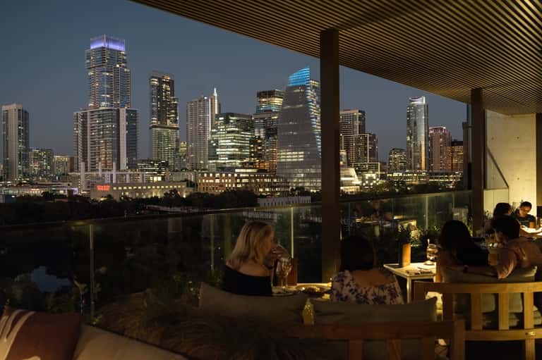 Upscale rooftop dining venue with floor-to-ceiling windows overlooking illuminated city skyline at dusk