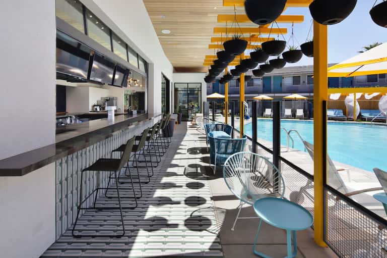 Poolside bar and seating area with yellow umbrellas and modern lounge chairs overlooking a bright blue pool