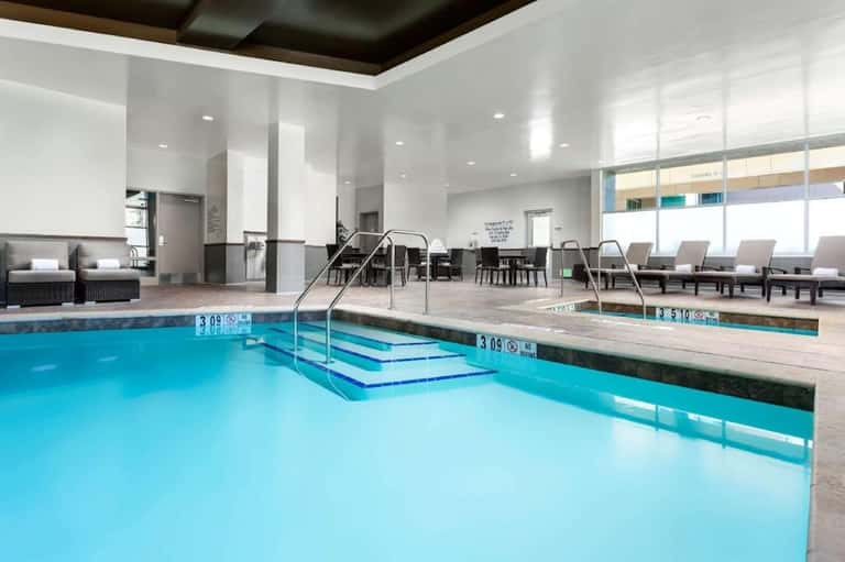 Indoor aquatic center with heated pool, spa, steps, seating area, and large windows