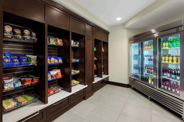 Hotel convenience store with dark wood snack shelves on left and refrigerated beverage cases on right