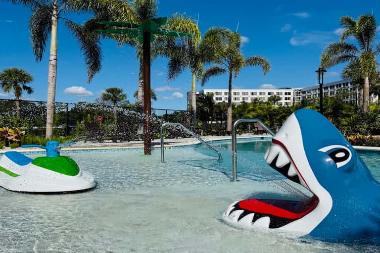 Shallow resort pool with colorful playful whale sculpture and palm trees in tropical setting