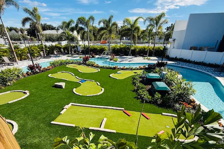 Mini golf course at resort with tropical landscaping, pools, and palm tree surroundings