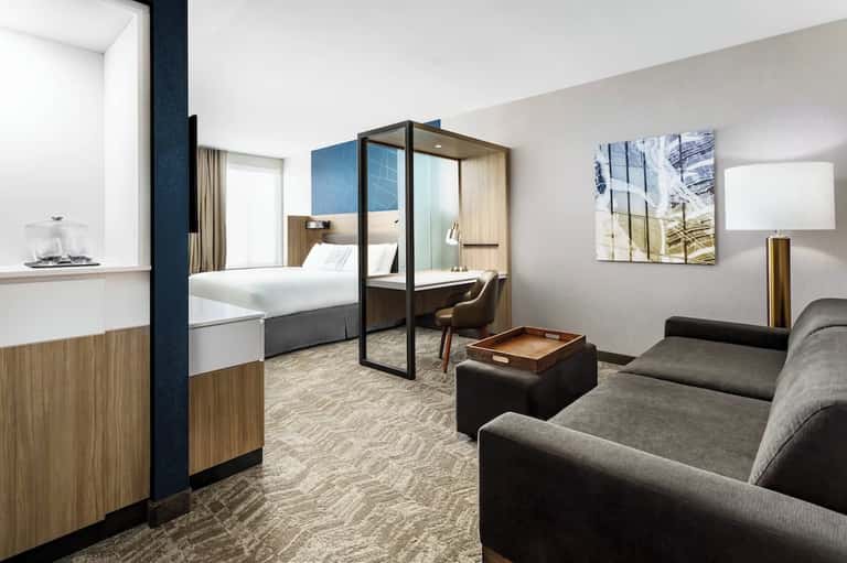 Modern hotel suite with four-poster bed, sitting area, wood accents, and contemporary design