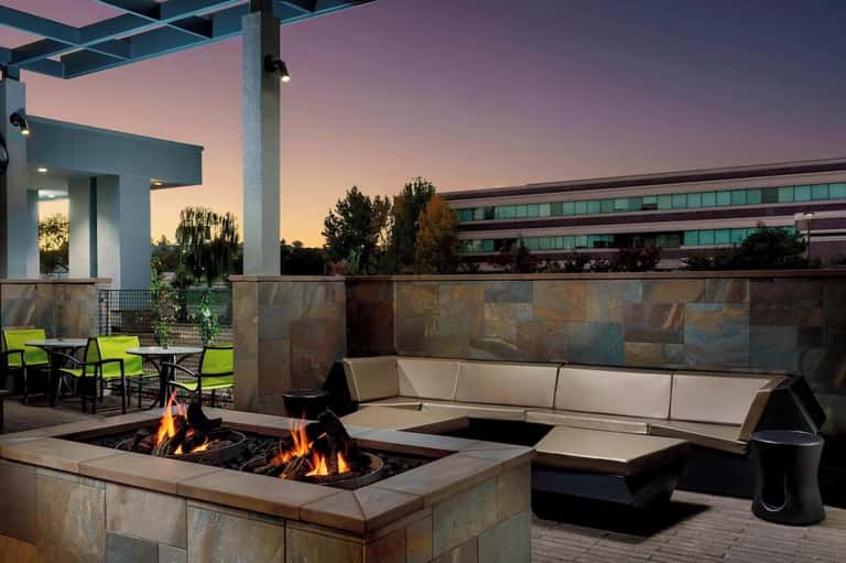 Rooftop terrace with fire pits, modern seating, stone walls, and sunset sky at dusk