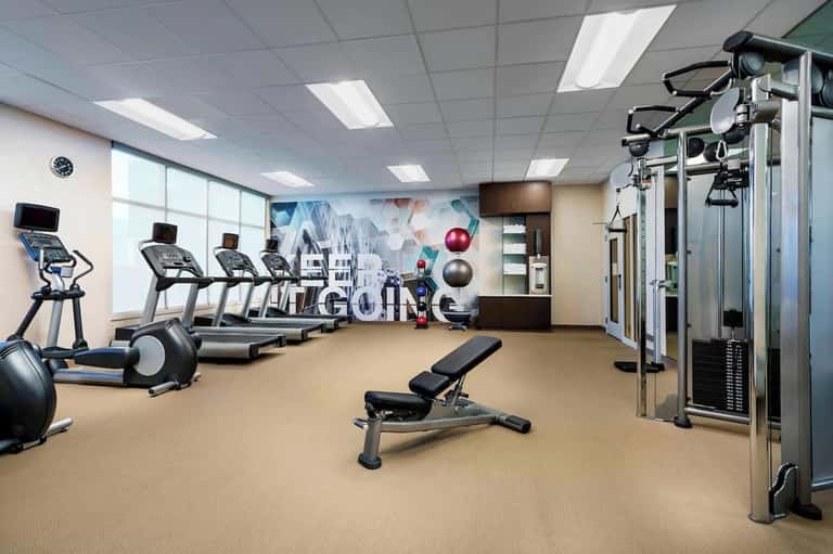Hotel gym with treadmills, elliptical machine, exercise balls, and cityscape wall mural with windows
