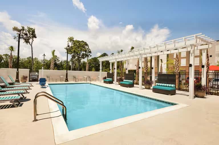 Resort swimming pool with white pergola shade structures and palm tree landscaping