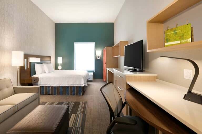 Modern hotel guest room with queen bed, desk, TV and teal accent wall