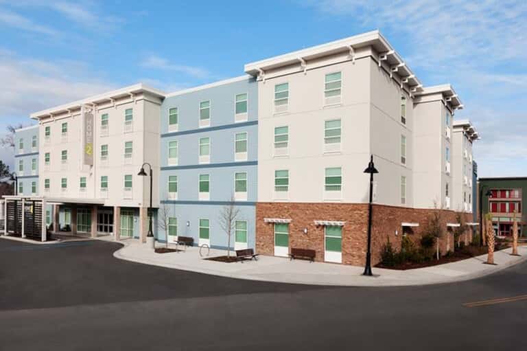 Modern four-story hotel building with light green and white facade and brick ground level