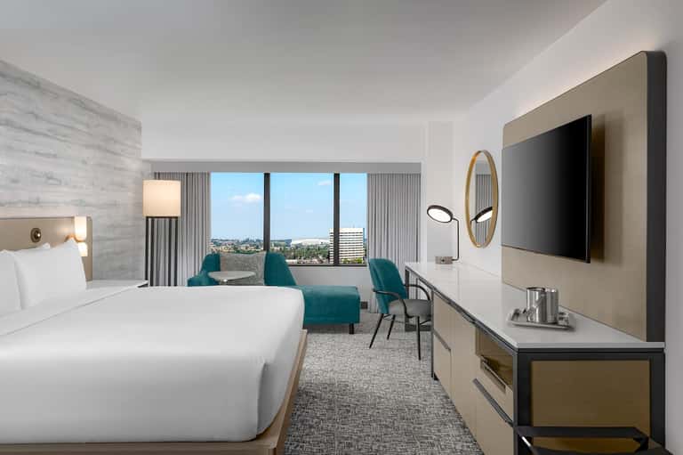 Modern hotel room with king bed, teal seating, and city skyline view