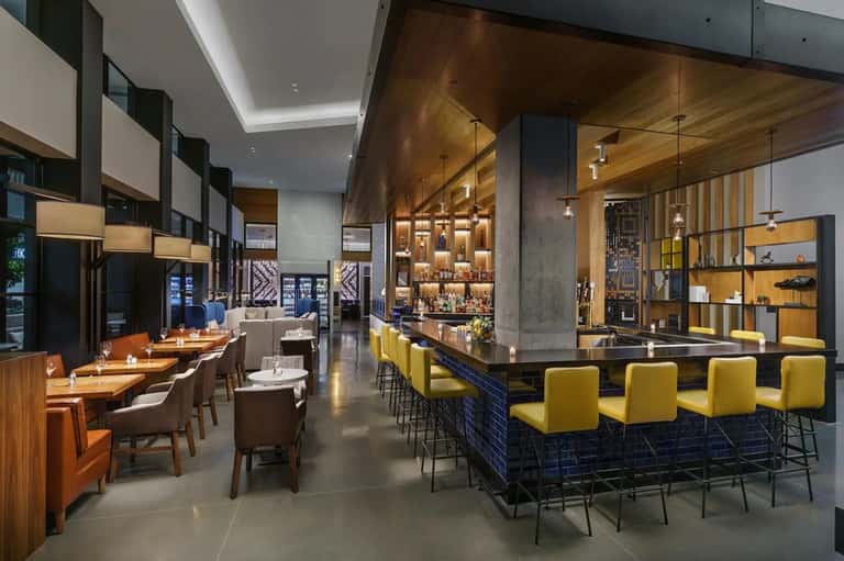 Modern hotel restaurant and bar with wood accents, yellow seating, and open design