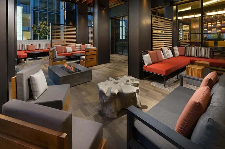 Contemporary lobby lounge with fireplace, red and gray seating, wood accents, and glass walls