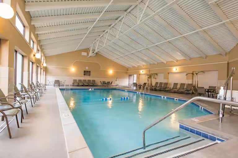 Indoor lap pool with pitched white ceiling, lane dividers, lounge chairs, and bright natural lighting