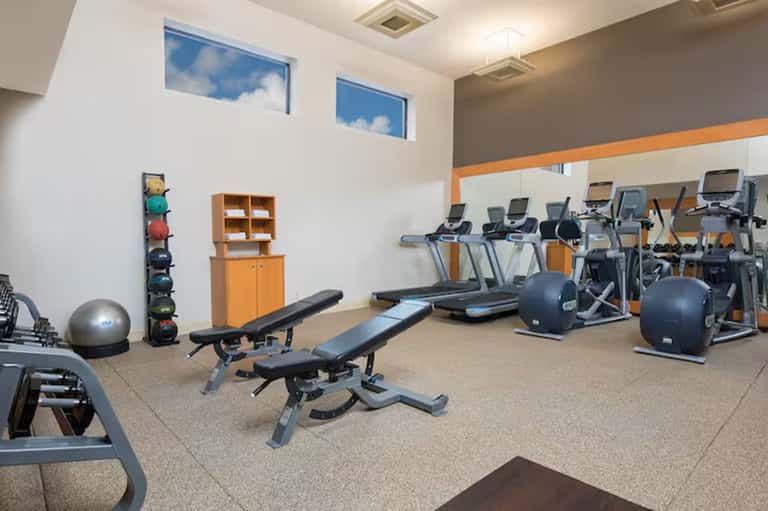 Fitness center with cardio equipment, weight machines, benches, and orange accent trim