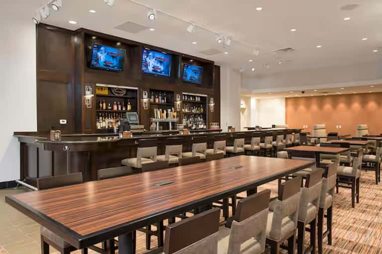 Hotel conference room with long wooden table, bar counter, and multiple screens