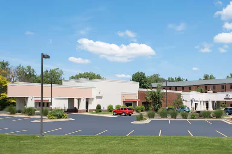 Modern medical facility exterior with pink and white facade, parking lot, and clear signage