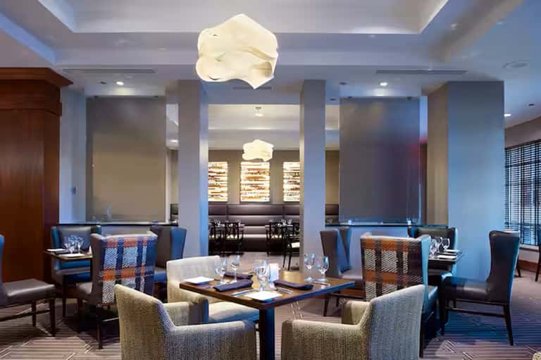 Upscale restaurant interior with cloud-shaped ceiling fixtures, blue accent chairs, neutral tones, and modern elegant design