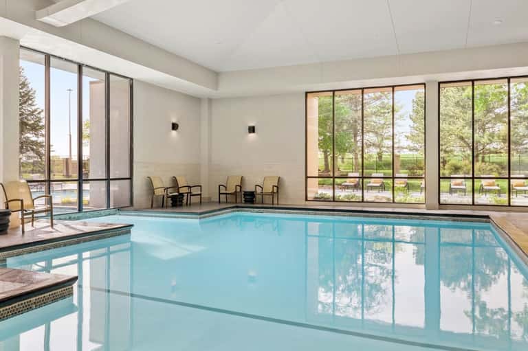 Indoor heated pool with large windows overlooking landscaped grounds and outdoor seating