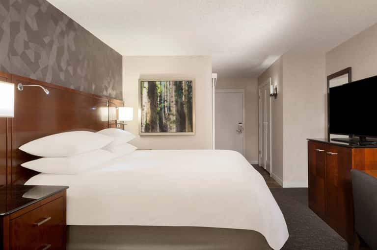 Hotel bedroom with queen bed, wood headboard, flat-screen TV, and neutral décor