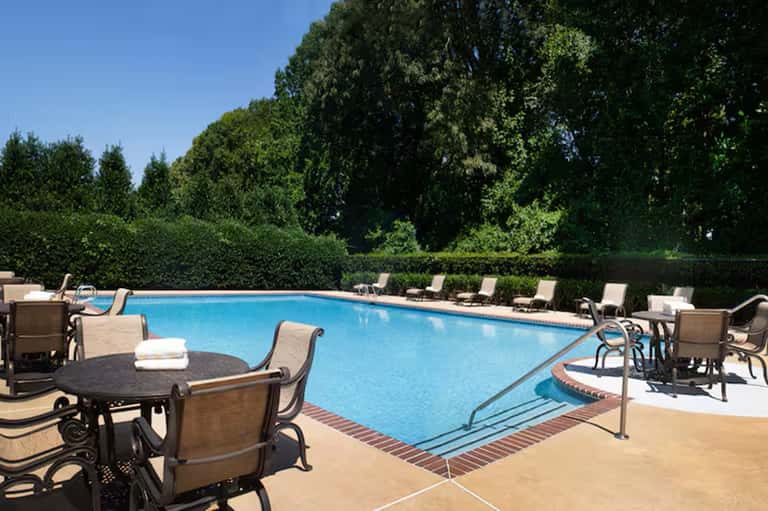 Resort pool with lounge chairs, umbrellas, and lush green trees providing shade