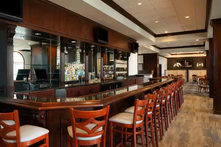 Traditional hotel bar with dark wood counter, red chairs, and full liquor display