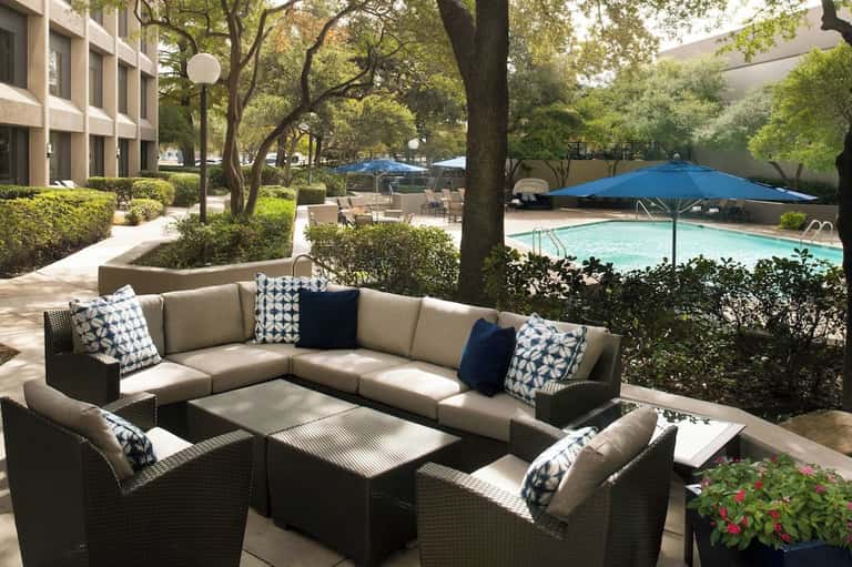 Outdoor seating area with sectional sofa, pool view, umbrellas, and mature trees