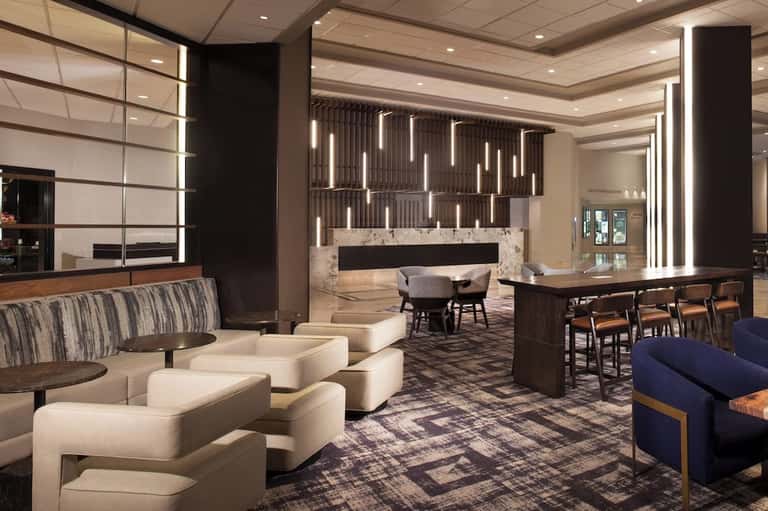 Modern hotel lobby with striped seating, geometric carpet, tall columns, and contemporary bar area