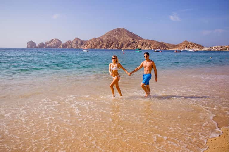 Fit couple running in shallow beach water with rocky island mountain in background