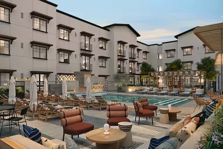 Contemporary pool courtyard with seating areas, umbrellas, and multi-story residential buildings at dusk